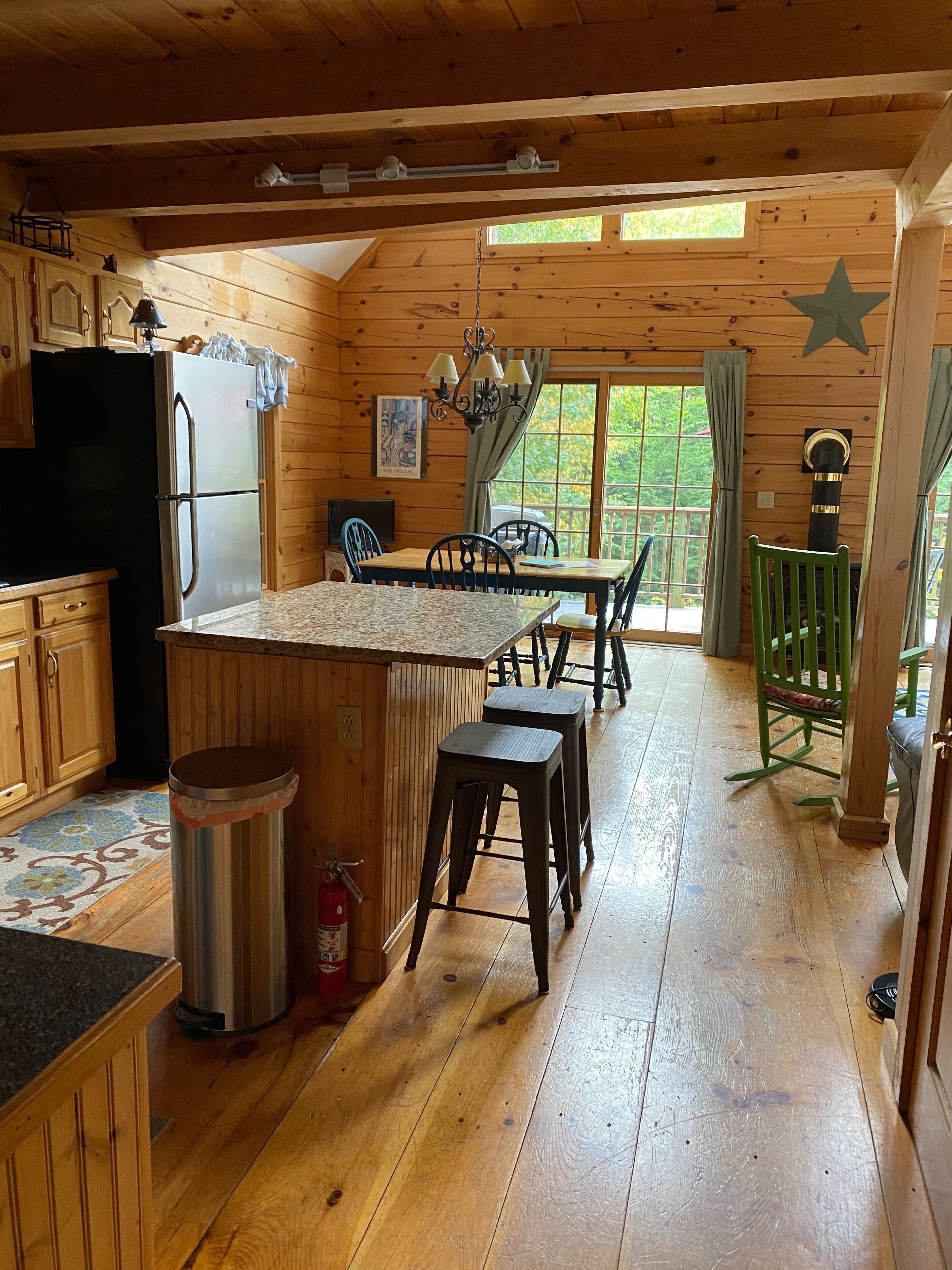 L’intérieur d’une cabane en bois comprend un coin cuisine équipé d’un réfrigérateur, une table à manger avec des chaises et un tabouret de bar.