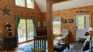 A cozy cabin interior with a fireplace, wooden walls, a dining area, and a seating area with a couch and chairs.