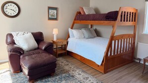 A room with a bunk bed, a leather armchair, a small bedside table with a lamp, and a wall clock. - Spacious Upstairs Loft (Miles City)