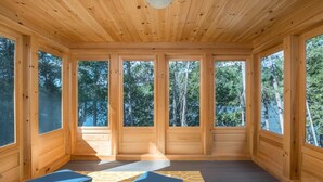 Une cabane en bois dotée de grandes fenêtres, d’un ventilateur de plafond et de deux fauteuils confortables.