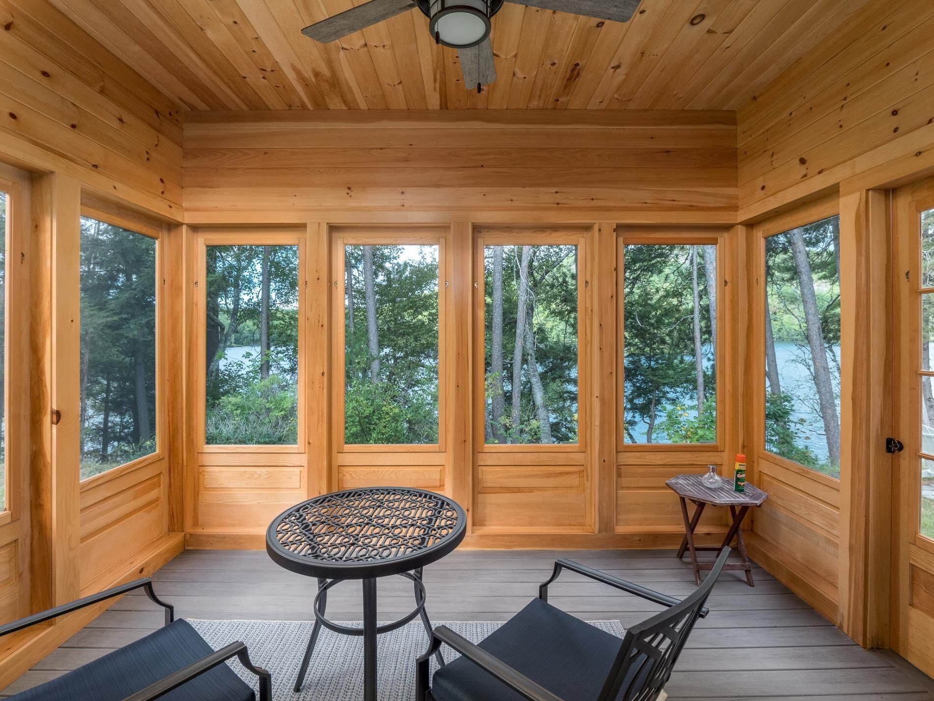 A wooden cabin with large windows, a ceiling fan, and a round table with chairs.