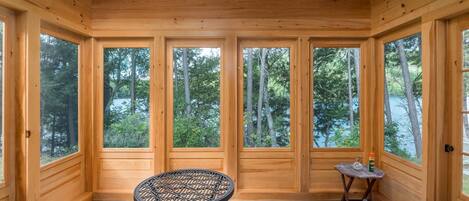A wooden cabin with large windows, a ceiling fan, and a round table with chairs.