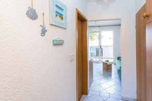Um corredor com uma porta de madeira, uma placa na parede com a inscrição 'THE BEACH' e vista para uma sala de jantar com mesa e cadeiras.