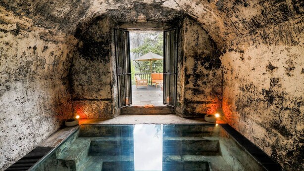 Eine gewölbte Steinstruktur, die zu einem Pool mit Glasboden und Treppen führt.