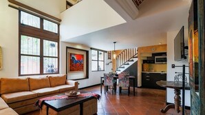 Ein großzügiger Wohnbereich mit Sofa, Couchtisch und Esstisch. Eine Treppe führt zu einer Küchenzeile mit modernen Geräten.