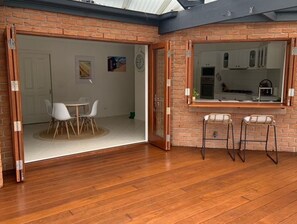 A room with a wooden floor, a dining area with a table and chairs, and a kitchen visible through a window.