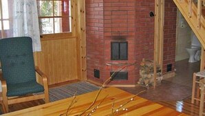 A wooden interior with a brick fireplace, a wooden staircase, and a green chair. - Honkatupa by Interhome (Ruovesi)