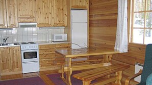 A kitchen with wooden cabinets, a white stove, a microwave, and a dining table with benches. - Honkatupa by Interhome (Ruovesi)