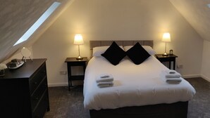 A bedroom with a sloped ceiling, two bedside lamps, a bed with white linens and black pillows, a small bedside table with a lamp, a dresser, and a television on a stand. - 4-bed Cottage in Portknockie, Near Cullen, Moray (Buckie)