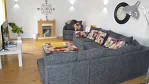 A modern living room with a grey sofa, colorful cushions, a fireplace, and a wall clock. - 4-bed Cottage in Portknockie, Near Cullen, Moray (Buckie)