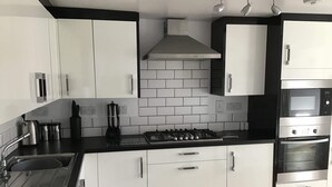 A modern kitchen with white cabinets, a black countertop, a stainless steel stove, and an oven. - 4-bed Cottage in Portknockie, Near Cullen, Moray (Buckie)