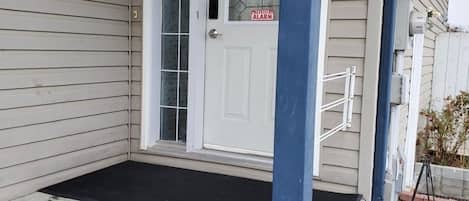 Una casa con puerta principal, un pequeño porche y un sistema de alarma visible.