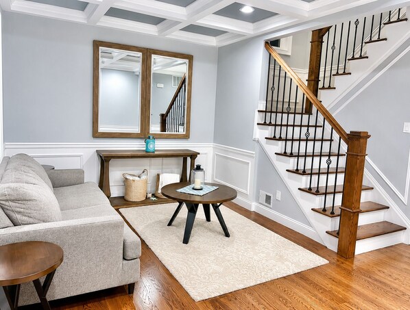 A living room with a sofa, a coffee table, a mirror, and a staircase.