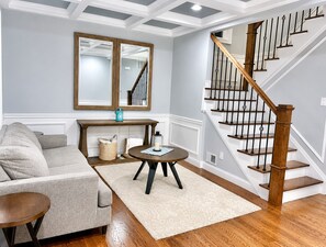 A living room with a sofa, a coffee table, a mirror, and a staircase. - Walk to Beach • Relaxing, Fully Equipped Home! (Long Branch)