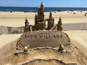 A sandcastle labeled 'PIER VILLAGE' with a beach and ocean in the background.