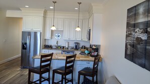 Una cocina moderna con armarios blancos, electrodomésticos de acero inoxidable y una isla central con taburetes de bar.