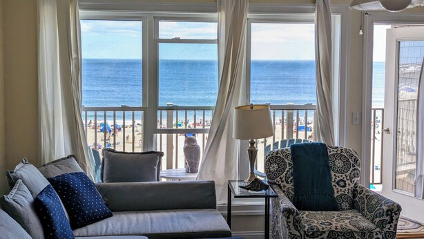 Una habitación con vista a la playa, un sofá, un sillón estampado y una lámpara.