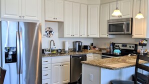 Una cocina moderna con armarios blancos, electrodomésticos de acero inoxidable, encimeras de granito y una isla central con asientos.