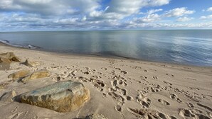 A beach with footprints and rocks, calm water, and a partly cloudy sky.