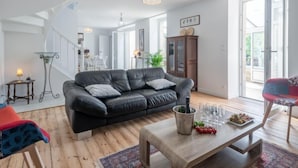 A modern living room with a black leather sofa, a wooden coffee table, and a staircase leading to an upper floor.