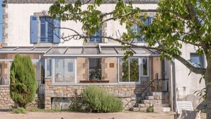 A stone house with a glass conservatory, outdoor seating, and a garden.
