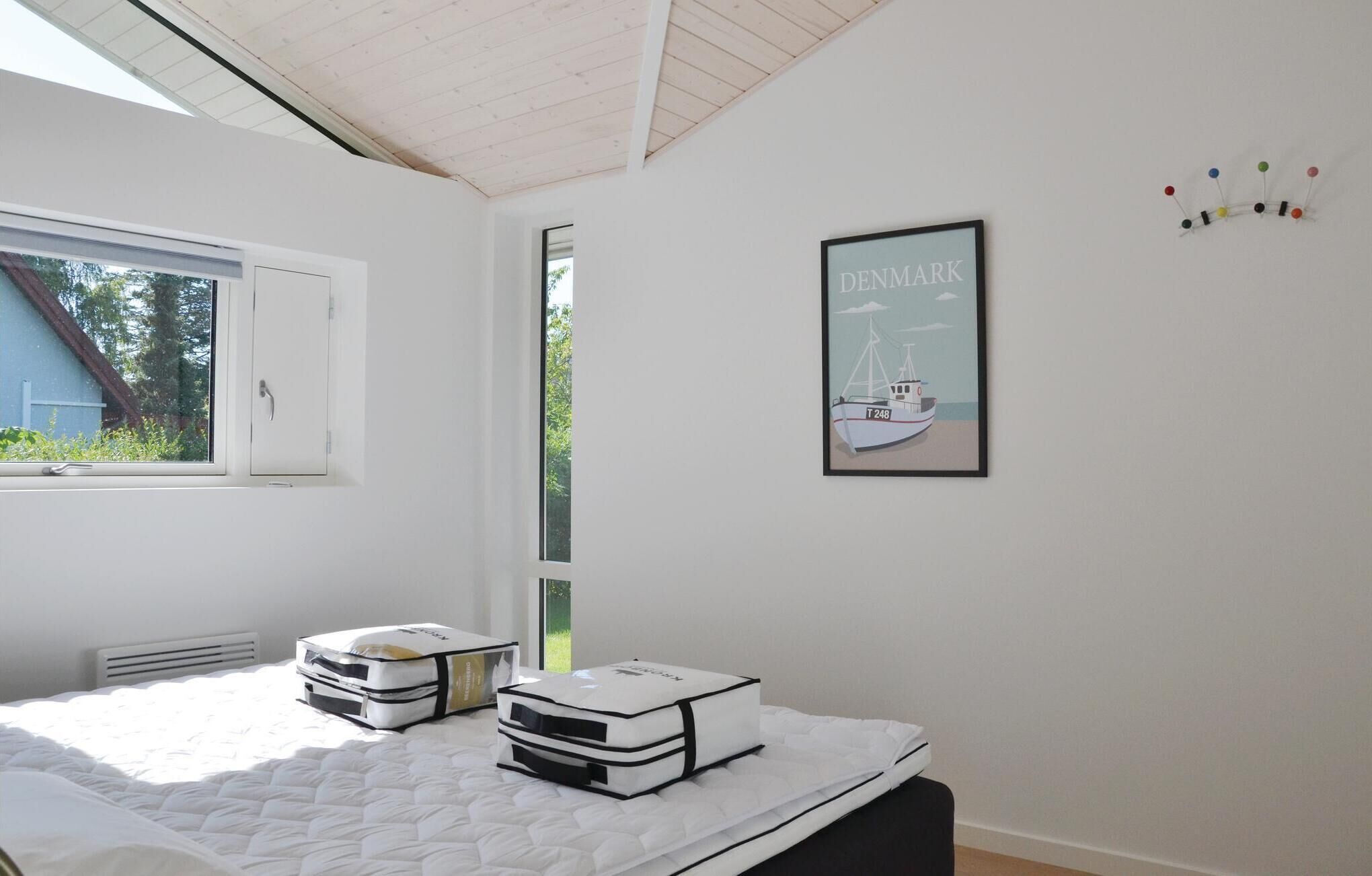 Een slaapkamer met een bed, een raam, een ingelijste afbeelding en een prikbord aan de muur.