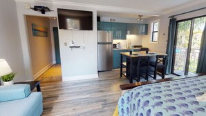 A modern kitchen with a built-in oven and microwave, a dining area with a table and chairs, and a large window offering a view of the outdoors. - Charming Studio Beach Getaway. Beachfront Pool, Near Restaurants, Activities (St. Pete Beach)