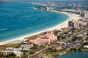 A coastal cityscape with a prominent pink building near the beach, a marina, and a densely populated urban area with high-rise buildings.