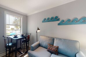A living room with a grey sofa, a dining table with chairs, a floor lamp, and decorative wall art.