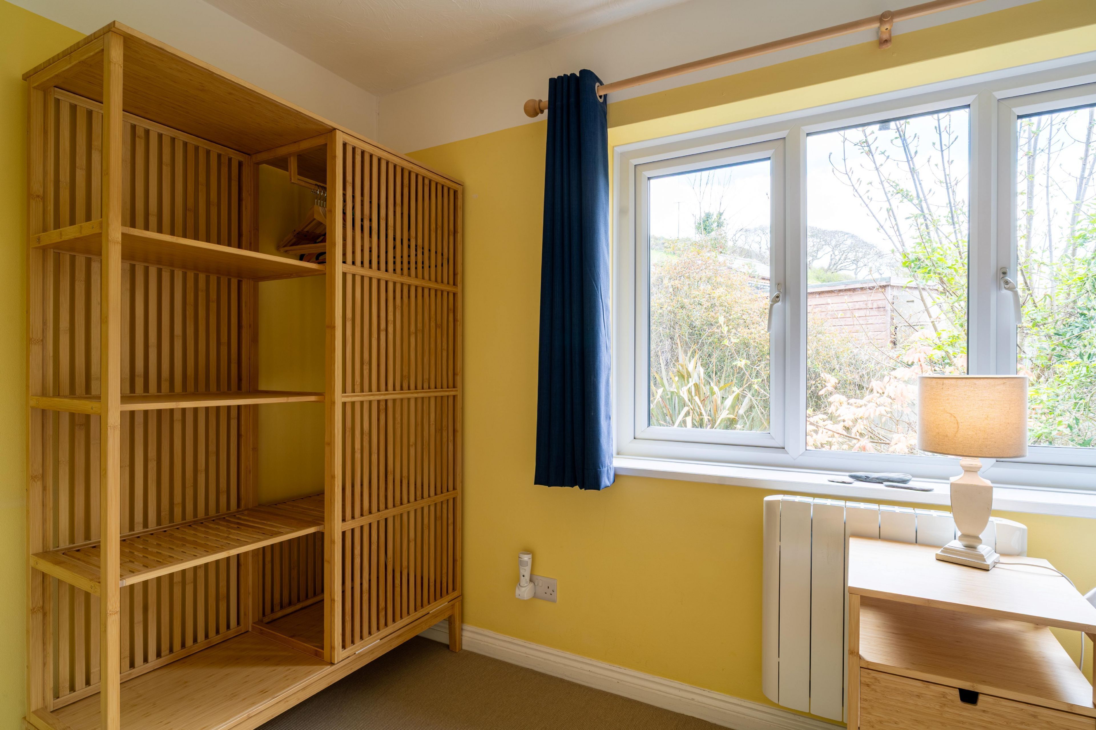 Ein Zimmer mit einem Holzbodenregal, einem Fenster mit Blick auf Grünflächen und einem Nachttisch mit einer Lampe.