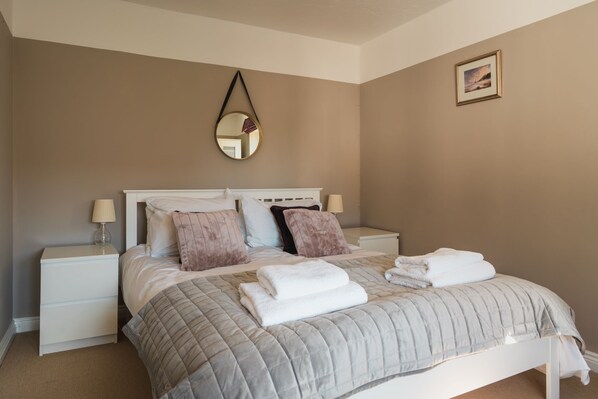 Une chambre à coucher avec un lit, des tables de chevet, un miroir et un tableau encadré au mur.