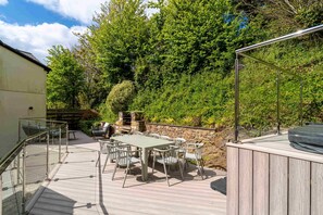 An outdoor deck with a table and chairs, a hot tub, and a stone barbecue grill.