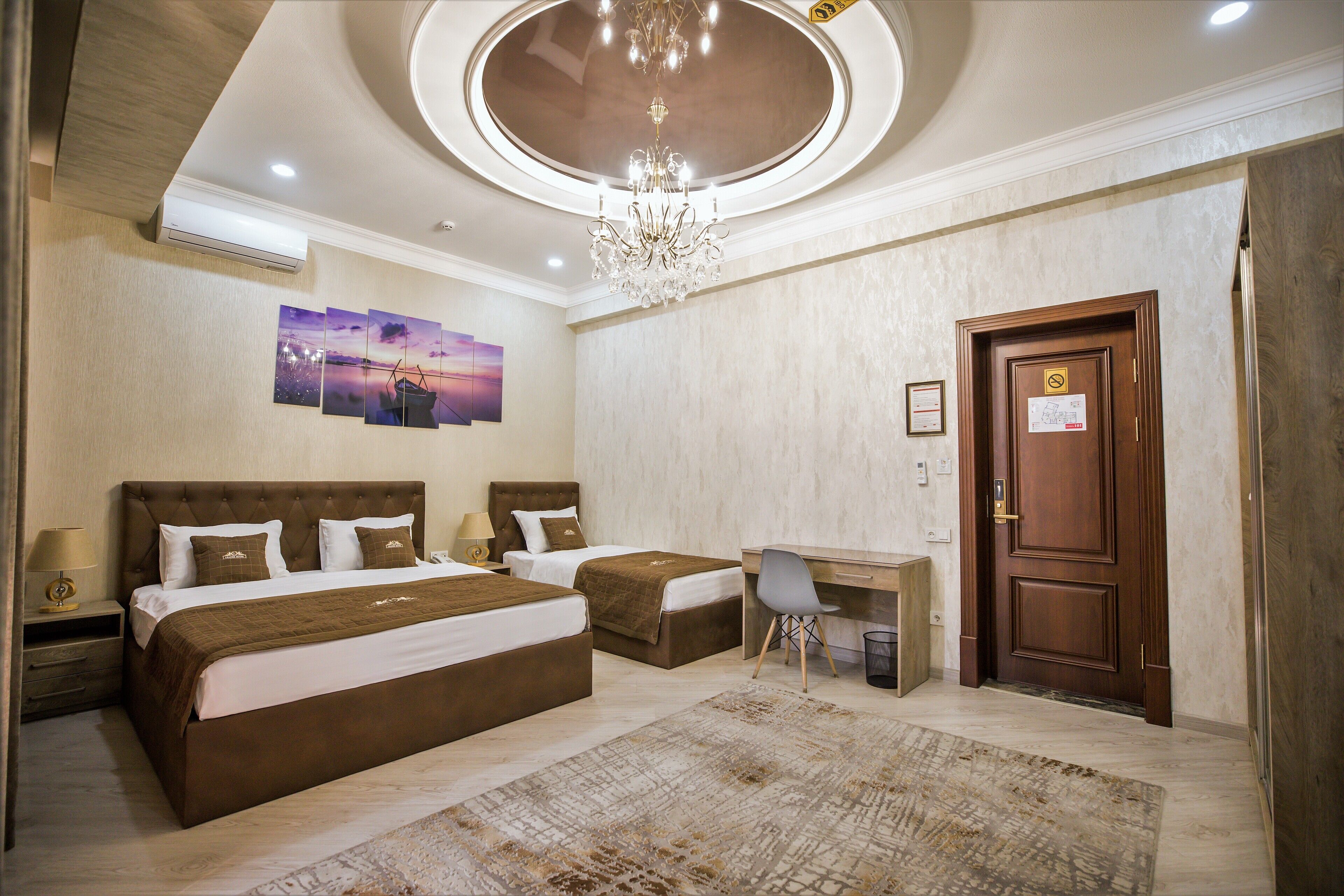 A hotel room with two beds, a desk, a chair, a chandelier, and artwork on the wall.