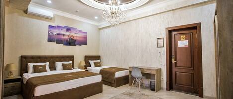 A hotel room with two beds, a desk, a chair, a chandelier, and artwork on the wall.