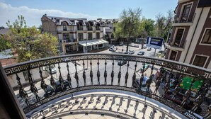 Et hotel med en gårdhave, der har et geometrisk flisemønster, et overdækket siddeområde samt udsigt til gaden med parkerede biler og bygninger i baggrunden.