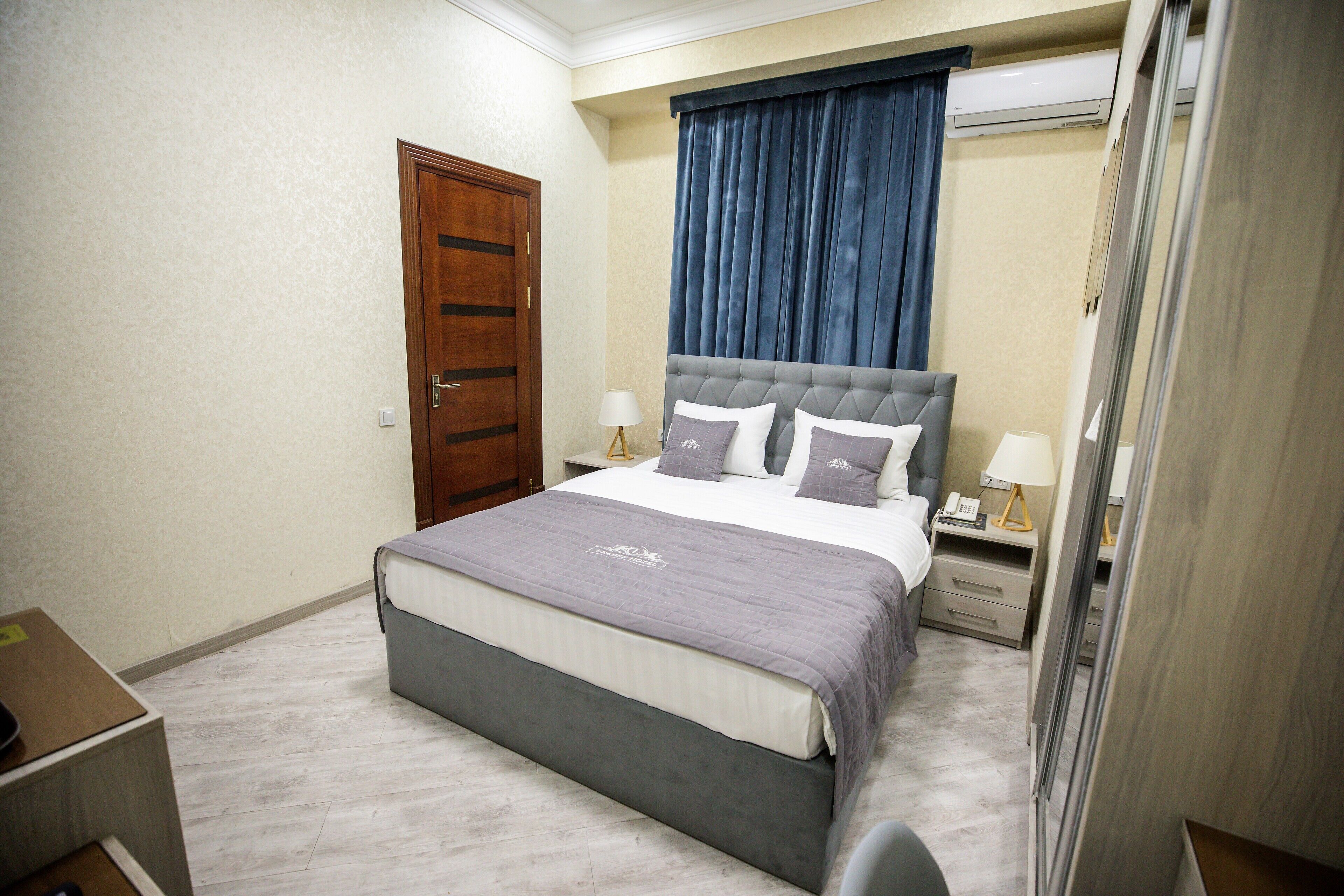 A neatly arranged bedroom with a large bed, a wooden door, a nightstand, and a desk.
