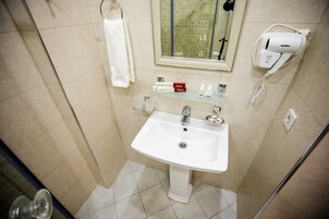 Un baño con lavamanos blanco, un espejo, toallero y secador de pelo en la pared.