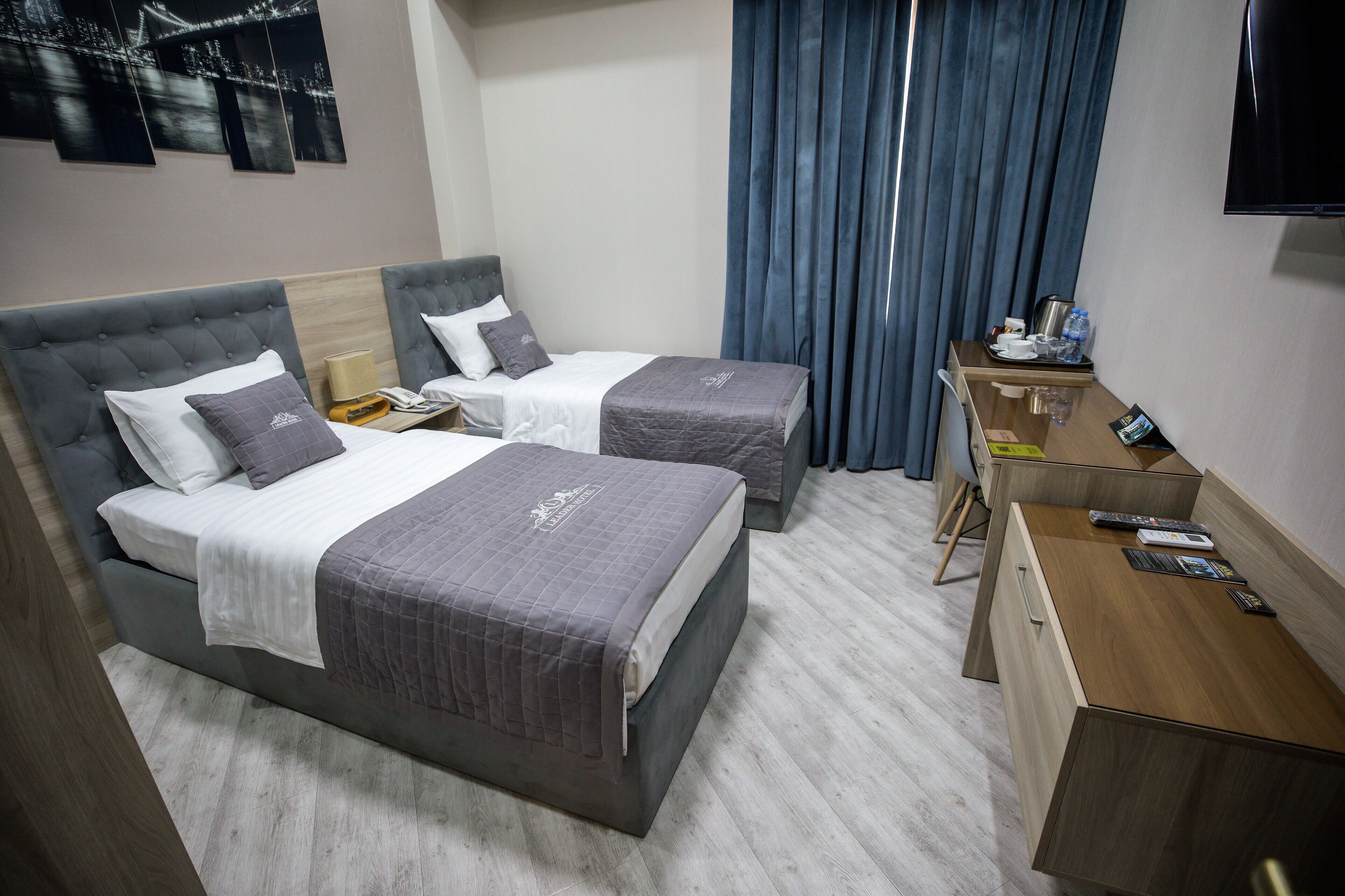 A hotel room with two beds, a desk, a TV, and a window with curtains.