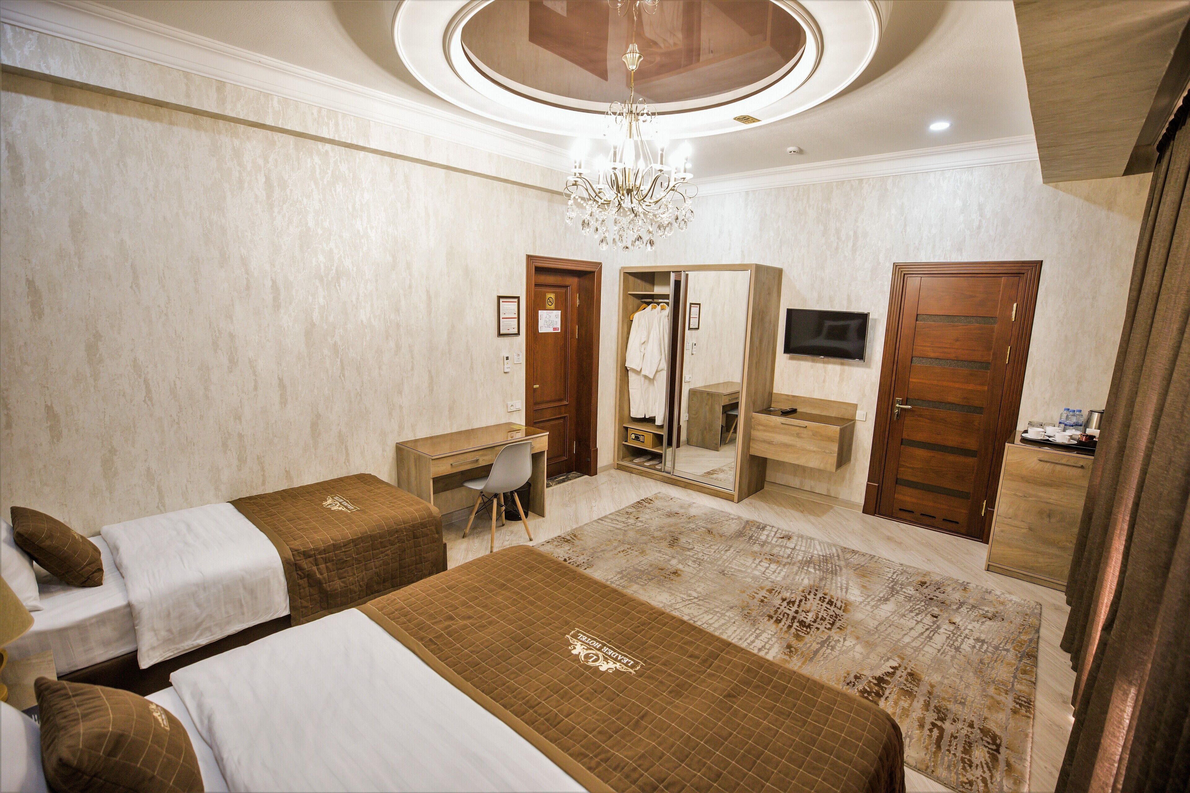 A hotel room with two beds, a desk, a chair, a TV, a mirror, and a wardrobe.