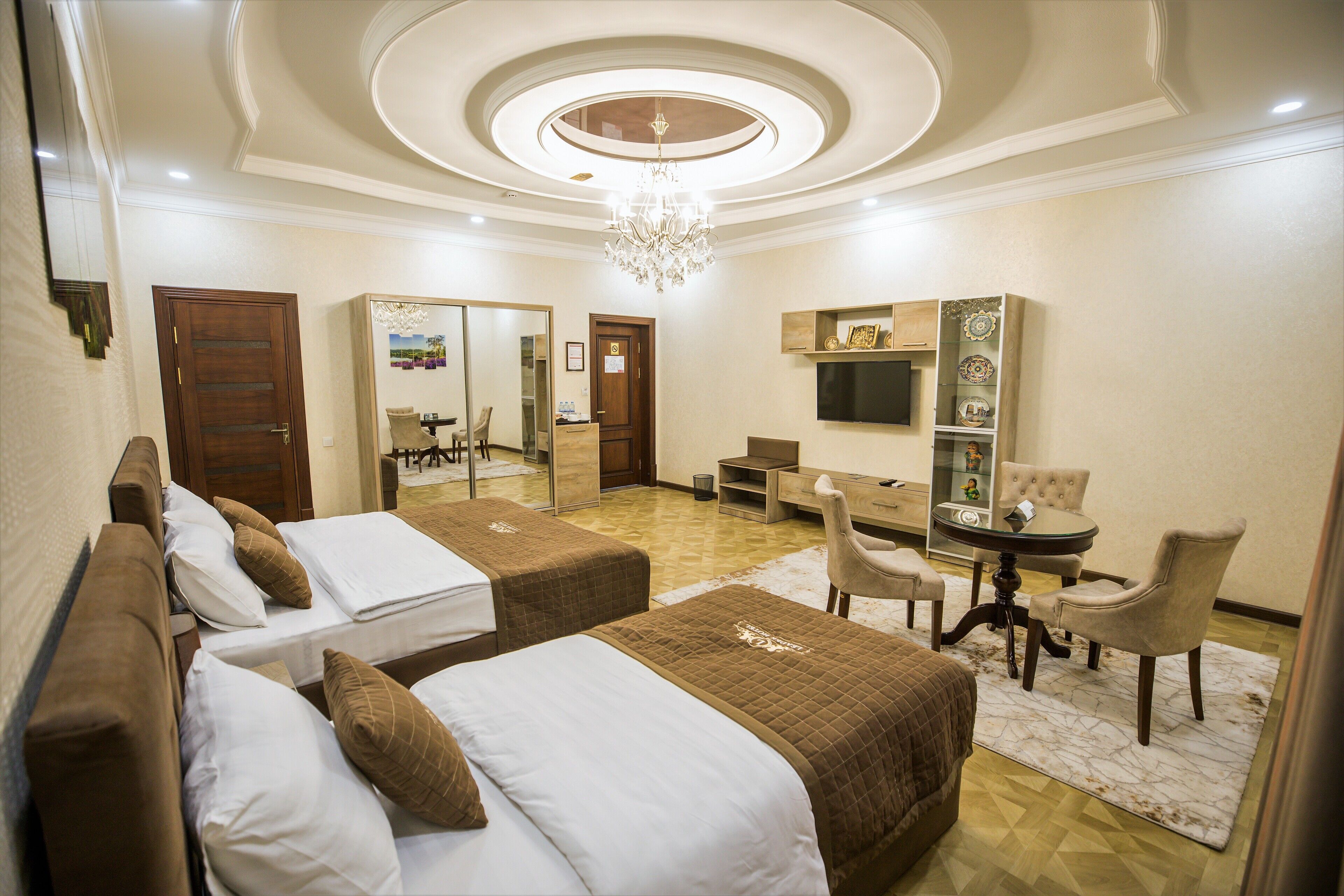 Quarto de hotel com duas camas, uma escrivaninha, uma cadeira, uma televisão e um candelabro.