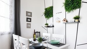 Ein moderner Essbereich mit weißen Stühlen, einem weißen Tisch und schwarzen Platzsets. Grüne Pflanzen stehen auf Regalen, und ein an der Wand befestigtes Schild trägt die Aufschrift "le boutique".