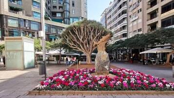A courtyard with a central tree sculpture surrounded by vibrant flower beds, set against a backdrop of modern buildings.