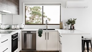 A modern kitchen with white cabinetry, stainless steel appliances, a large window, and a view of trees outside.