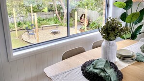 A dining area with a large window, a table set with plates, a vase of flowers, and a hanging light fixture.