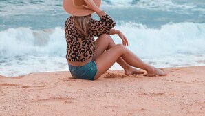 A person sitting on a sandy beach with the ocean in the background.