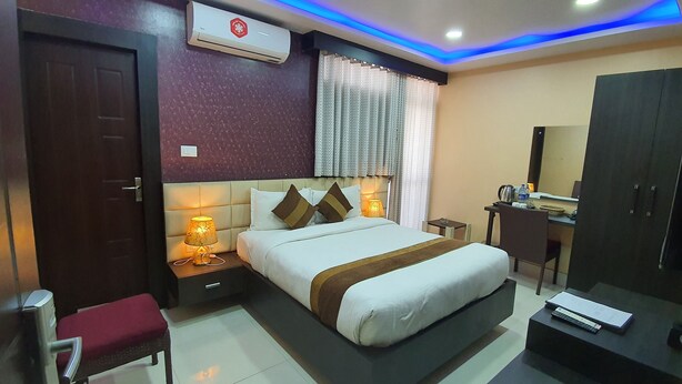 A hotel room with a bed, bedside table with a lamp, a desk with a chair, a wardrobe, and a mirror.