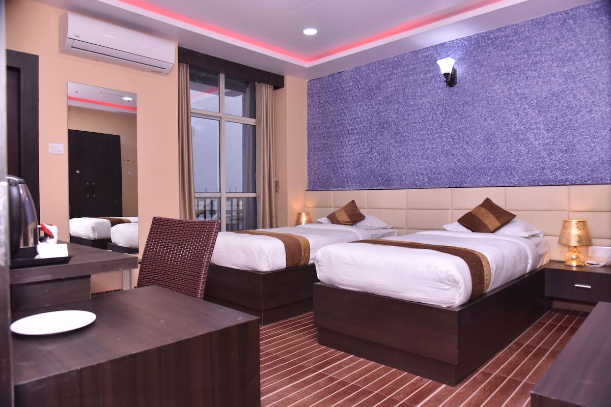 Ein Hotelzimmer mit zwei Betten, einem Schreibtisch, einem Stuhl, einem Fenster und einer Wandleuchte.