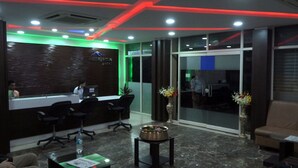 A reception area with a modern design, featuring a reception desk, black office chairs, a small table with a vase of flowers, and a brown leather couch.