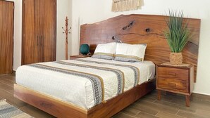 Un dormitorio con una cama de madera, una mesita de noche, un adorno colgante de macramé y una planta en maceta.