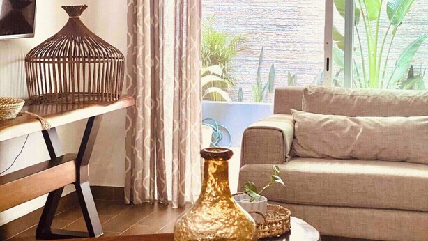 Sala de estar con sofá, televisión, ventana grande con cortinas y vistas a zonas verdes.